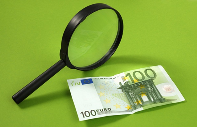 Lupa powiększająca leżąca obok banknotu o nominale 100 euro. Grafika symbolizująca badanie audytowe, analizę i sprawdzanie procesów przeciwdziałania praniu pieniędzy.