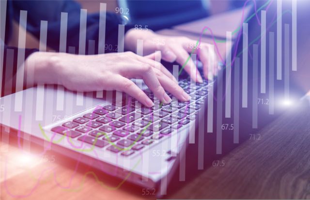 Dłonie na laptopie na tle wykresów słupkowych i linii – grafika obrazująca analizę danych w programie komputerowym np. w systemie AML i KYC.
